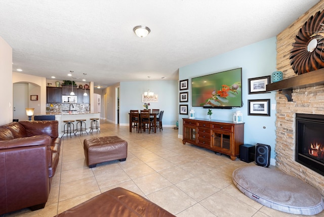 2659 Vista Manzano Loop NE, Rio Rancho, NM 87144 - living area with light tile patterned flooring, arched walkways, a stone fireplace, a chandelier, and a textured ceiling