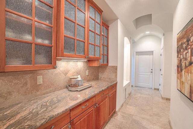 4110 Waterwillow Pl NW, Albuquerque, NM 87120 - kitchen with light stone counters, arched walkways, glass insert cabinets, brown cabinetry, and decorative backsplash