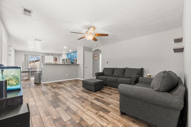 1227 Desert Paintbrush Loop, Rio Rancho, NM 87144 - living room featuring arched walkways, light wood-type flooring, a textured ceiling, a ceiling fan, and baseboards