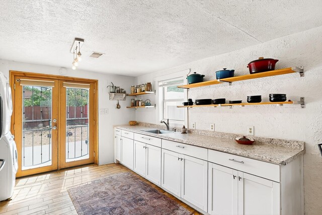 1508 Barelas Rd SW, Albuquerque, NM 87102 - kitchen featuring open shelves, a sink, stacked washer / drying machine, light wood-style flooring, and a textured ceiling