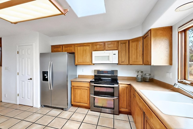 1704 Quail Run Ct NE, Albuquerque, NM 87122 - kitchen with appliances with stainless steel finishes, a sink, a skylight, light tile patterned floors, and brown cabinets
