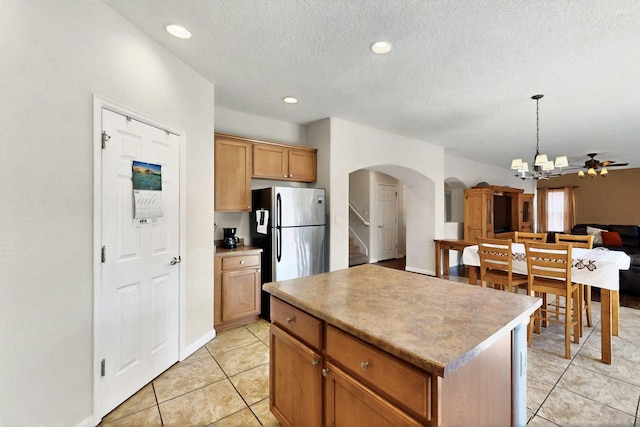 1412 Wind Ridge Dr NW, Albuquerque, NM 87120 - kitchen featuring arched walkways, freestanding refrigerator, light tile patterned floors, open floor plan, and a center island