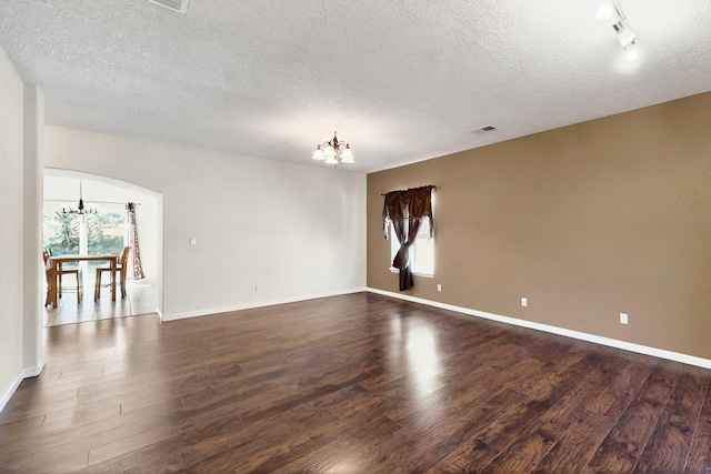 1412 Wind Ridge Dr NW, Albuquerque, NM 87120 - empty room featuring a chandelier, dark wood-style flooring, arched walkways, and a textured ceiling
