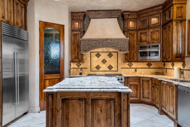 9301 Black Farm Ln NW, Albuquerque, NM 87114 - kitchen featuring stainless steel appliances, premium range hood, backsplash, and light stone counters