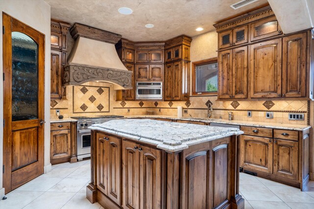 9301 Black Farm Ln NW, Albuquerque, NM 87114 - kitchen with high end stainless steel range, premium range hood, light tile patterned floors, a center island, and tasteful backsplash