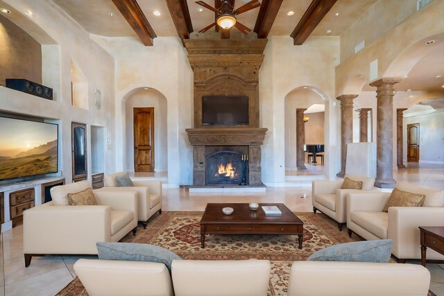 9301 Black Farm Ln NW, Albuquerque, NM 87114 - tiled living room with arched walkways, a high ceiling, beam ceiling, ceiling fan, and a warm lit fireplace
