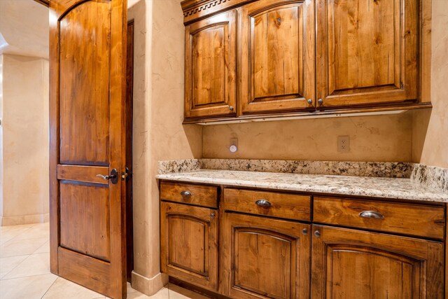 9301 Black Farm Ln NW, Albuquerque, NM 87114 - kitchen with brown cabinetry, light stone counters, and light tile patterned floors