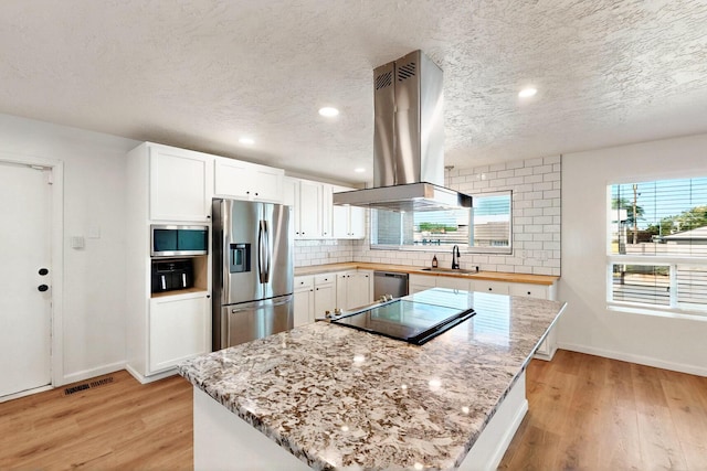 2912 Alcazar St NE, Albuquerque, NM 87110 - kitchen with appliances with stainless steel finishes, island range hood, light wood finished floors, a sink, and a textured ceiling