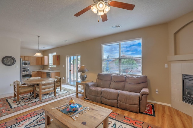 1921 Cortina Loop SE, Rio Rancho, NM 87124 - living area with light wood-type flooring, a ceiling fan, a tile fireplace, baseboards, and a textured ceiling