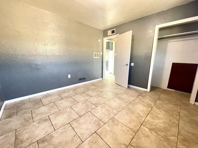 820 Apache Ave NW, Albuquerque, NM 87102 - unfurnished bedroom with a closet, a textured ceiling, a textured wall, tile patterned flooring, and baseboards
