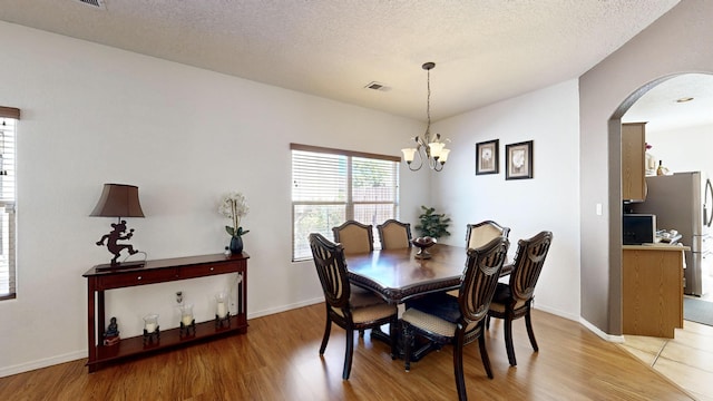 3032 Cochiti St NE, Rio Rancho, NM 87144 - dining space with arched walkways, light wood-style floors, a chandelier, a textured ceiling, and baseboards