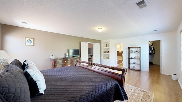 3032 Cochiti St NE, Rio Rancho, NM 87144 - bedroom featuring a walk in closet, wood finished floors, a textured ceiling, ensuite bath, and baseboards
