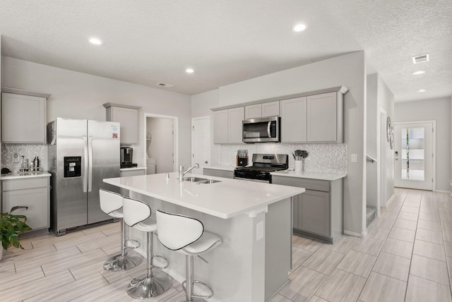 684 Turmalina Dr SE, Rio Rancho, NM 87124 - kitchen with stainless steel appliances, gray cabinetry, a sink, backsplash, and a center island with sink