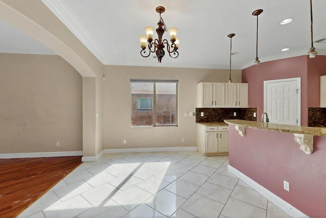 6505 Basket Weaver Ave NW, Albuquerque, NM 87114 - kitchen with crown molding, a breakfast bar area, light stone counters, arched walkways, and a chandelier