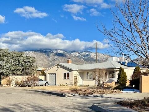 9722 Apache Ave NE, Albuquerque, NM 87112 - single story home with a mountain view, a chimney, an attached garage, and stucco siding