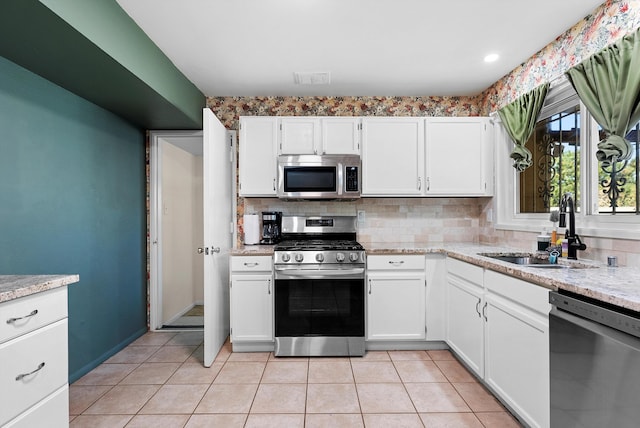 7609 Hannett Ave NE, Albuquerque, NM 87110 - kitchen featuring stainless steel appliances, a sink, decorative backsplash, white cabinetry, and light tile patterned floors
