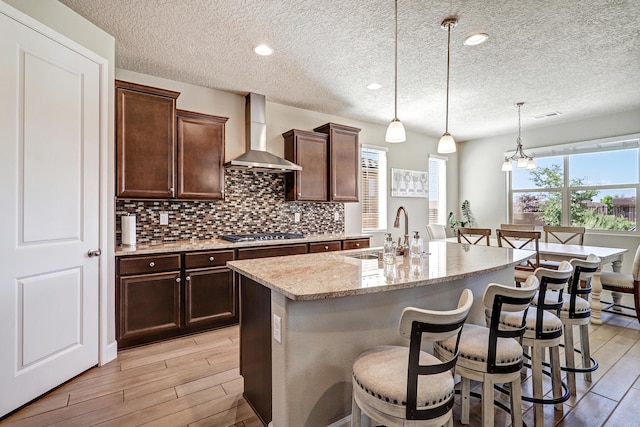 6240 Redroot St, Albuquerque, NM 87120 - kitchen with wall chimney exhaust hood, a sink, stainless steel gas cooktop, light wood-style floors, and a textured ceiling
