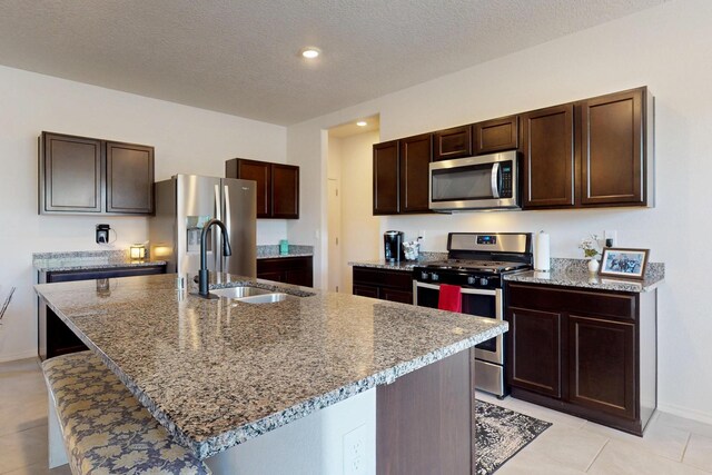2317 Solara Loop NE, Rio Rancho, NM 87144 - kitchen with appliances with stainless steel finishes, dark brown cabinets, a kitchen island with sink, light stone counters, and a textured ceiling
