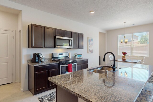 2317 Solara Loop NE, Rio Rancho, NM 87144 - kitchen featuring stainless steel appliances, dark brown cabinetry, a chandelier, a textured ceiling, and dark stone countertops