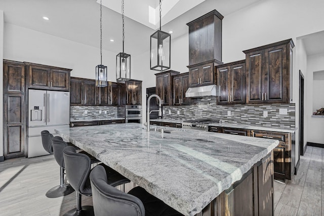 11 Del Cerro Ct, Los Lunas, NM 87031 - kitchen featuring stainless steel appliances, dark brown cabinetry, hanging light fixtures, a spacious island, and under cabinet range hood