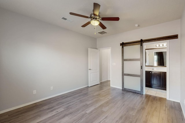9624 Basalt Peak Dr NW, Albuquerque, NM 87114 - unfurnished bedroom with light wood-style floors, a barn door, baseboards, ensuite bathroom, and ceiling fan