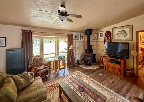 34 Halcon Rd, Ramah, NM 87321 - living room featuring wood finished floors, a wood stove, and a ceiling fan