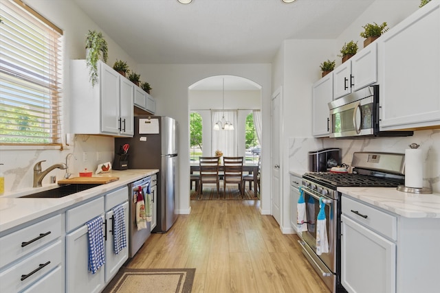 2115 Cortina Loop SE, Rio Rancho, NM 87124 - kitchen featuring appliances with stainless steel finishes, a sink, arched walkways, light wood finished floors, and tasteful backsplash