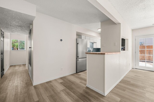 1616 Vail Pl SE, Albuquerque, NM 87106 - kitchen with freestanding refrigerator, a textured ceiling, light wood-type flooring, a peninsula, and white cabinets