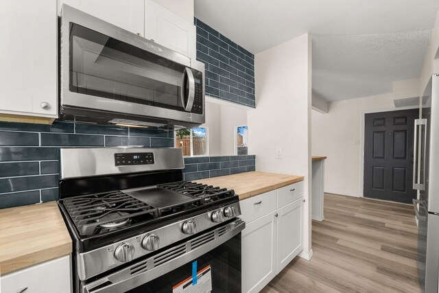 1616 Vail Pl SE, Albuquerque, NM 87106 - kitchen featuring butcher block counters, stainless steel appliances, white cabinets, light wood-style floors, and decorative backsplash