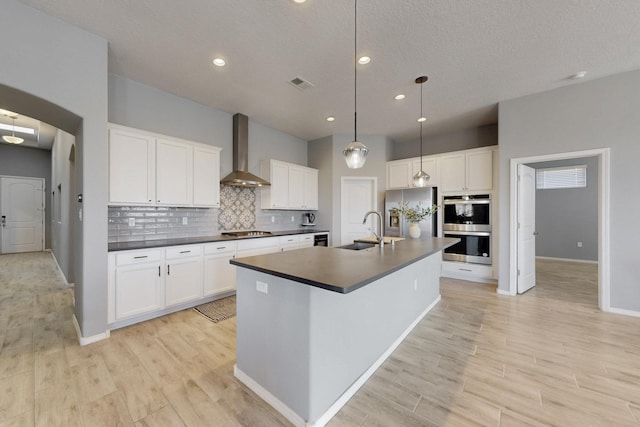 7037 Cleary Loop NE, Rio Rancho, NM 87144 - kitchen featuring wall chimney range hood, a sink, stainless steel appliances, dark countertops, and light wood-type flooring