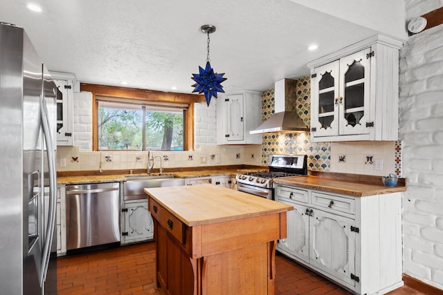 234 Horton Ln NW, Albuquerque, NM 87114 - kitchen featuring butcher block countertops, appliances with stainless steel finishes, wall chimney range hood, brick floors, and a textured ceiling