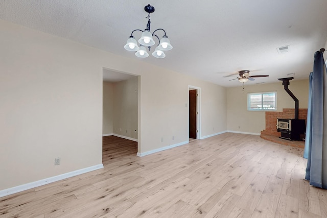 508 San Juan De Rio Dr SE, Rio Rancho, NM 87124 - unfurnished living room featuring a wood stove, light wood finished floors, a ceiling fan, baseboards, and a chandelier