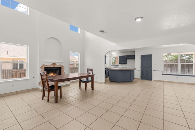 10504 W Connemara Ave SW, Albuquerque, NM 87121 - dining space with arched walkways, a tile fireplace, light tile patterned floors, plenty of natural light, and a towering ceiling