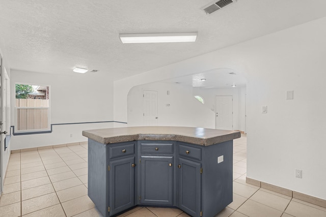 10504 W Connemara Ave SW, Albuquerque, NM 87121 - kitchen with arched walkways, blue cabinets, light tile patterned floors, dark countertops, and a textured ceiling