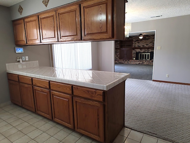 4111 El Cajon Ct SE, Rio Rancho, NM 87124 - kitchen featuring brown cabinetry, a textured ceiling, a peninsula, light carpet, and light tile patterned floors