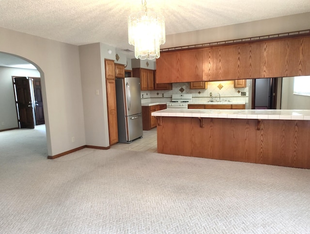4111 El Cajon Ct SE, Rio Rancho, NM 87124 - kitchen featuring freestanding refrigerator, tile countertops, brown cabinets, arched walkways, and a textured ceiling