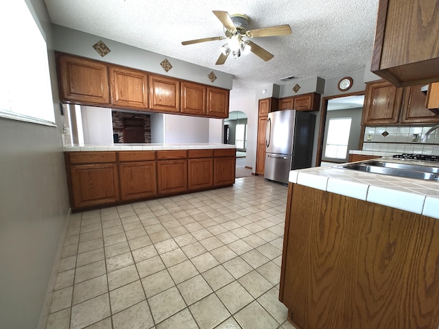 4111 El Cajon Ct SE, Rio Rancho, NM 87124 - kitchen featuring freestanding refrigerator, tile counters, brown cabinets, ceiling fan, and a peninsula