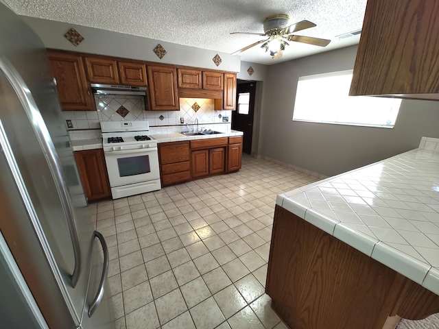 4111 El Cajon Ct SE, Rio Rancho, NM 87124 - kitchen with gas range gas stove, under cabinet range hood, a sink, freestanding refrigerator, and decorative backsplash