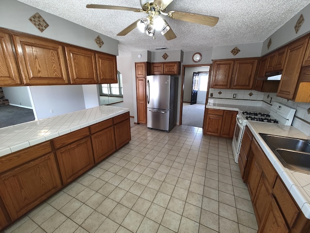 4111 El Cajon Ct SE, Rio Rancho, NM 87124 - kitchen featuring freestanding refrigerator, white gas range oven, a ceiling fan, brown cabinetry, and a textured ceiling