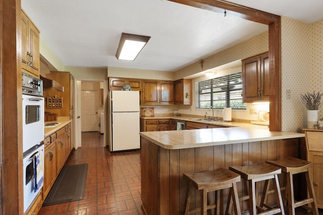 8480 Osuna Rd NE, Albuquerque, NM 87111 - kitchen with white appliances, wallpapered walls, brick patterned flooring, a peninsula, and light countertops