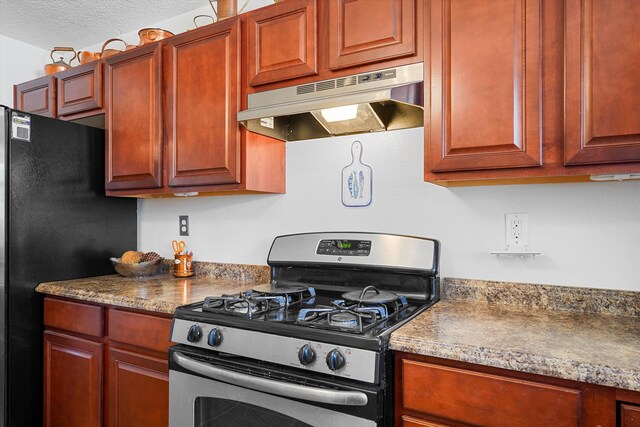 1951 Corta Rustica, Los Lunas, NM 87031 - kitchen featuring stainless steel gas range oven, under cabinet range hood, freestanding refrigerator, a textured ceiling, and reddish brown cabinets