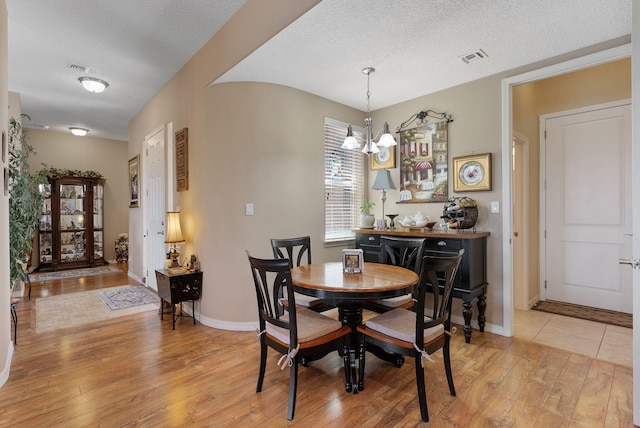 4210 Agave Ct SW, Los Lunas, NM 87031 - dining room featuring light wood-style flooring, a chandelier, a textured ceiling, and baseboards