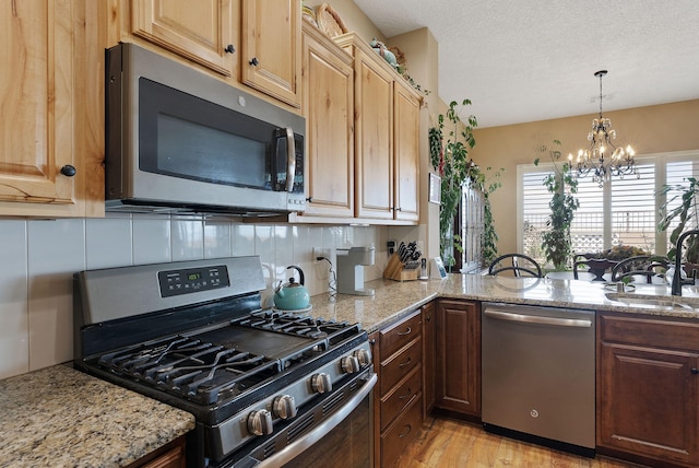 4210 Agave Ct SW, Los Lunas, NM 87031 - kitchen with appliances with stainless steel finishes, a chandelier, a sink, tasteful backsplash, and light stone countertops