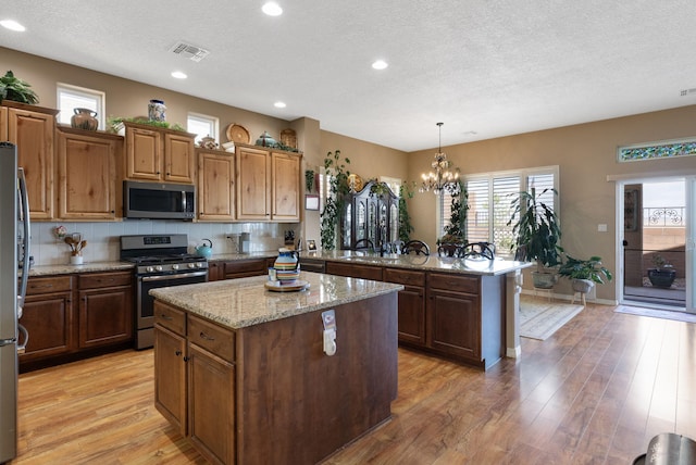 4210 Agave Ct SW, Los Lunas, NM 87031 - kitchen featuring appliances with stainless steel finishes, a textured ceiling, a peninsula, a kitchen island, and light wood-style floors