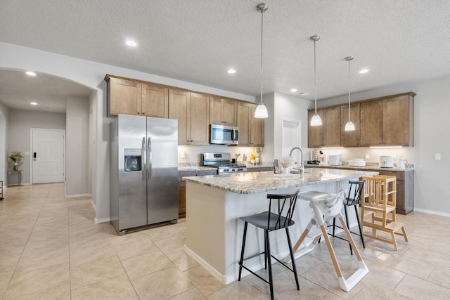3217 Vatapa Rd NE, Rio Rancho, NM 87144 - kitchen with appliances with stainless steel finishes, arched walkways, a center island with sink, recessed lighting, and light stone counters
