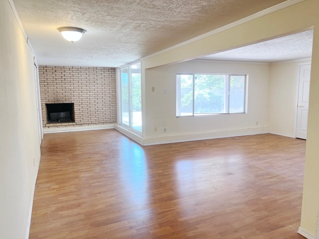 10008 Greene Ave NW, Albuquerque, NM 87114 - unfurnished living room featuring a textured ceiling, light wood-style flooring, ornamental molding, a brick fireplace, and baseboards