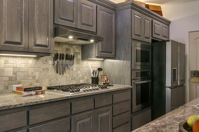 31 Express Blvd, Sandia Park, NM 87047 - kitchen with stainless steel appliances, under cabinet range hood, dark brown cabinetry, tasteful backsplash, and light stone counters