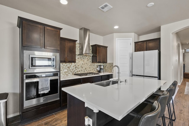 9035 S Sky St NW, Albuquerque, NM 87114 - kitchen with stainless steel appliances, wall chimney exhaust hood, a sink, a center island with sink, and dark wood finished floors