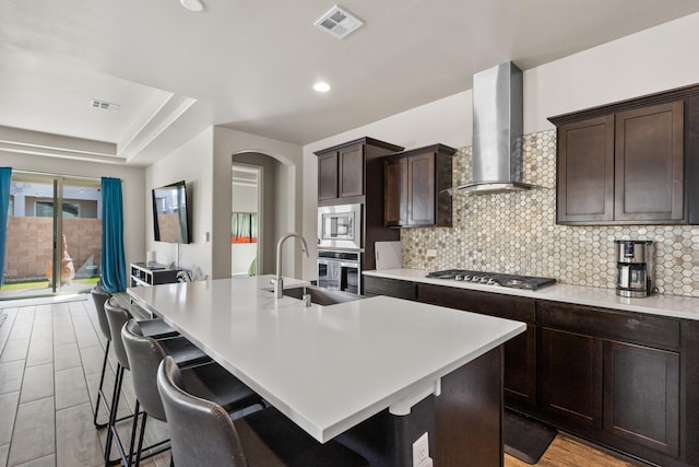 9035 S Sky St NW, Albuquerque, NM 87114 - kitchen featuring wall chimney range hood, appliances with stainless steel finishes, a sink, backsplash, and a kitchen breakfast bar
