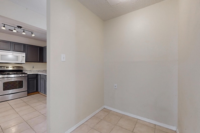 2815 Quail Pointe Dr NW, Albuquerque, NM 87120 - kitchen featuring white microwave, stainless steel gas range, light tile patterned flooring, baseboards, and a textured ceiling